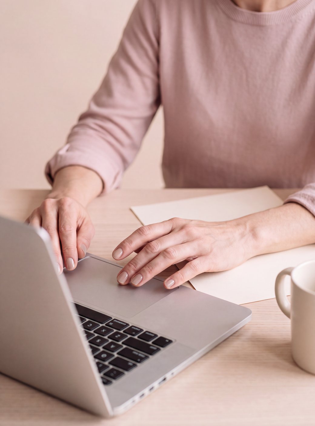 Hände auf der Tastatur eines Laptops, daneben eine Tasse